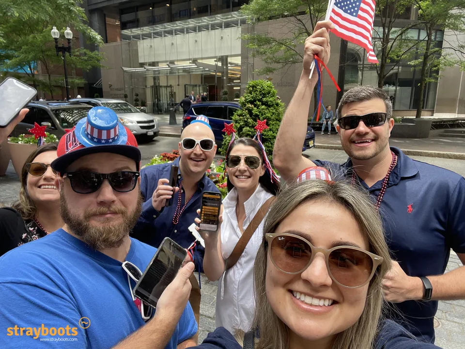 A Boston team takes a group selfie with phones and red, white and blue accessories.